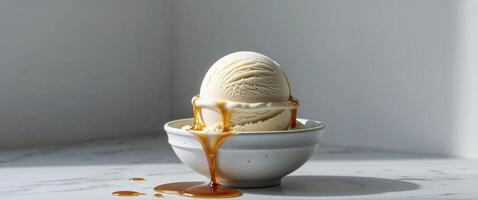 Vanilla ice cream scoop in ceramic bowl with drizzle of caramel syrup set on marble table for gourmet frozen dessert presentation photo