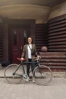 Rider in tweed attire poses with retro bicycle outside unique architectural building photo