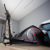 Modern Elliptical Trainer in the Room at Home. Concept of Exercising at Home, fitness. Copy space for text photo
