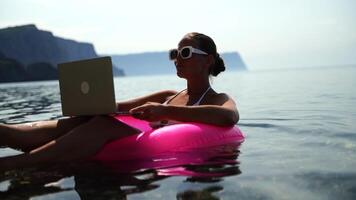 Work Remote Beach. Woman floats on the water using laptop for relaxation on a summer holiday. video