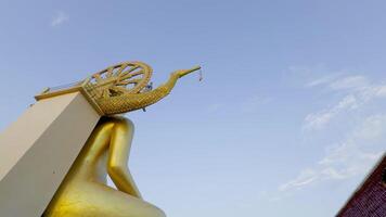 A medium shot captures a passenger airplane in flight against a clear blue sky, juxtaposed with a partial view of the large, golden Big Buddha statue on Koh Samui, Thailand. The intricate details of video