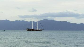 A wide shot shows a sailing ship moving smoothly across the calm, slightly rippled sea under engine power, its sails lowered. video