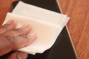 Cleaning a smartphone screen with a tissue on a wooden table photo