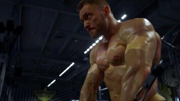 muscular man engages in a challenging exercise routine at a gym showcasing strength and focus. The environment is well lit emphasizing his physique and determination video