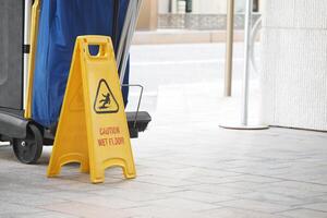 Caution sign indicating wet floor near cleaning equipment outside photo
