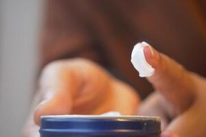Hands are shown applying cream from a container, focusing on skincare photo
