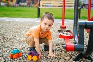 Little toddler boy playing with cars on pebbles on the playground. Boy two or three years old. Toddlerhood childhood concept. Residential complex. photo
