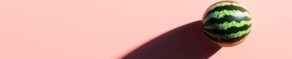 Minimalist composition featuring a single round watermelon on a pink background photo