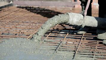 Close-up of concrete being poured from industrial hose onto reinforced rebar grid, Wet cement mix spreading to form foundation slab during early stage of construction video