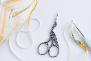 Crochet tools and yarn ball with bird shaped scissors on white surface photo