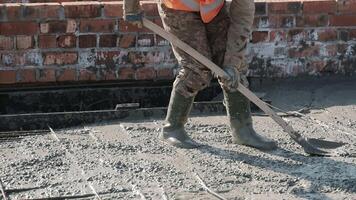 Construction worker levels wet concrete using shovel during slab formation on rebar frame, Close-up of manual labor in early stage of building foundation under sunny sky video