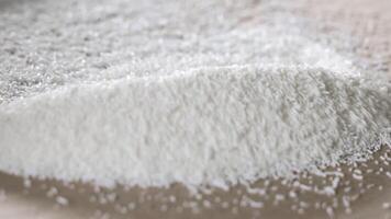 White plastic polymer granules spread and leveled with a wooden stick on cardboard, Close-up of raw material handling for plastic production or injection molding video