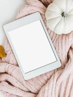 Pastel colored tablet mockup with cozy knitted blanket and white pumpkin for autumn design photo