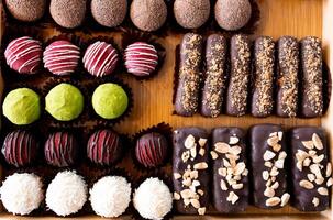Assorted chocolate truffles and bars on a wooden tray with variety of toppings photo