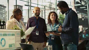 Relaxed multiethnic coworkers in office having fun chatting while reviewing documents, analyzing metrics. Smiling multiracial colleagues talking, working together, looking over paperwork, camera B video