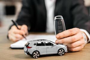 Man signing car insurance document or lease paper. Writing signature on contract or agreement. Buying or selling new or used vehicle. Car keys on table. Warranty or guarantee. Banner photo