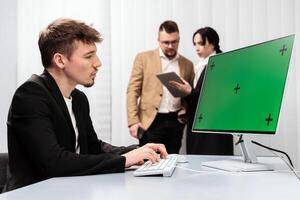 A group of successful businessmen in the office with a desktop computer featuring a Chroma Key green screen. Concept discussing deal completion, income growth, and strategic company development photo