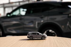 Small car model toy is placed on a table against blurred auto background. Premium car buying experience that combines expert guidance with high-class service in an elegant setting. Copy space, banner photo
