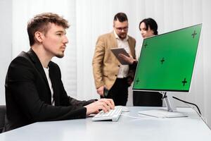 A group of successful business people in the office with a desktop computer featuring a Chroma Key green screen. Concept discussing deal completion, income growth, and strategic company development photo