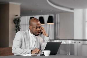 Man focusing on information in computer working alone in modern office. Focused adult african businessman in formal wear with laptop, listening learning education course conference. photo
