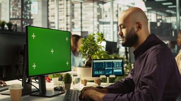 Man in office reviewing financial graphs on green screen PC, analyzing key performance indicators. Employee looking over data trends and strategic insights on chroma key computer, camera B video