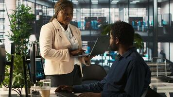 Worker in office receiving feedback from management executive looking over work done on laptop. African american manager in workspace giving tasks to employee, providing necessary data, camera A video