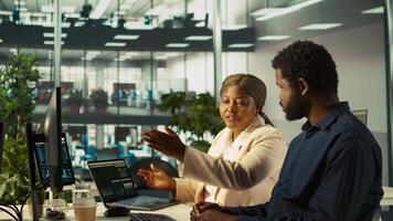 Supervisor in office discussing with employee about key performance indicators for revenue, profitability and operational efficiency. African american manager supervising employee at work, camera B video