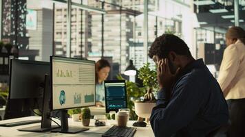 Worker feeling painful headache while working, suffering burnout while rushing to finish tasks before deadline. African american man in office having migraine after working overtime, camera B video