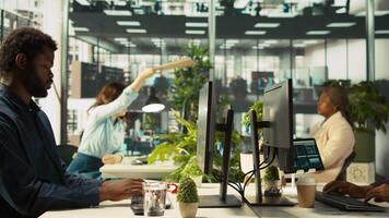 Accountant in busy workplace talking with colleagues while inputting financial figures on PC. Employee working in modern office chatting with coworkers while crosschecking data, camera B video