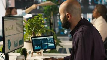 Accountant in busy workplace talking with colleagues while inputting financial figures on PC. Employee working in modern office chatting with coworkers while crosschecking data, camera A video