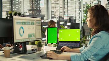 Office clerk uses chroma key devices to read data statistics on display after audit. Employee at work using green screen laptop and tablet to check progress done on commissioned project, camera B video