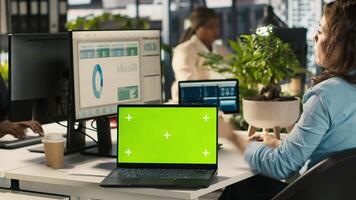 Green screen mockup laptop next to accountant inputting financial figures on PC after checking reports. Chroma key notebook next to businesswoman working in office, crosschecking data, camera A video