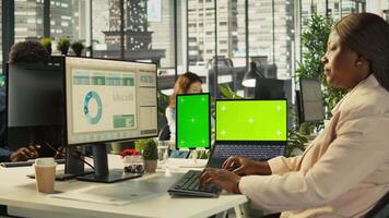 Mockup tablet and laptop in office used by employee working on company administrative tasks. Chroma key devices on desk used by worker reviewing business data metrics, camera B video