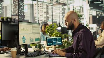Accountant in office inputting financial figures on PC, giving report files to coworkers. Arab man in workplace crosschecking data on computer, giving documents to colleagues, camera B video