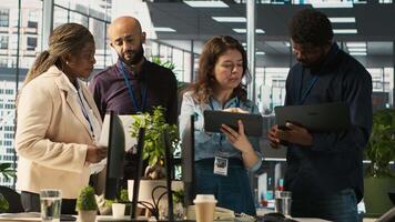 Multiethnic coworkers looking over revenue figures on tablet in diverse office. Multiracial colleagues doing brainstorming, comparing company statistical numbers, working hard to finish job, camera A video