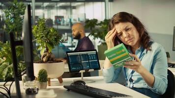 Stressed woman in office feeling painful headache while working, suffering burnout, reading medication box instructions. Employee having migraine after working overtime to finish project, camera B video