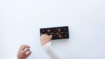 Child Hands reach for assorted chocolates in elegant box on white surface video