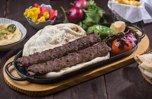 Iraqi Kebab meat Platter served on a tray with grilled meat kebabs koobideh, pita bread, hummus, and various sides isolated on wooden table side view of Middle Eastern dish photo