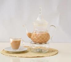 hot milk tea with teapot served in glass cup isolated on background side view of hot drink Karak Tea photo