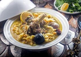 Iraqi Meat Tashreeb served in a bowl with tender meat, a rich yellow broth, lemon, and ingredients isolated on wooden table side view of Middle Eastern stew photo