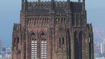 Aerial view of Liverpool Cathedral, showcasing its Gothic architecture, towering spire, and ornate windows with cityscape and waterfront cranes visible. video