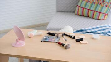 Close-up of a wooden table with assorted makeup items including brushes, mirror, eyeshadow palette, and skincare tools in a cozy indoor setting. photo