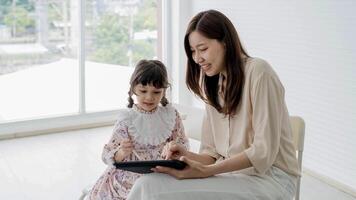 Mother and daughter using digital tablet together with stylus, smiling and learning happily at home in bright room, sharing fun screen time and creativity. photo