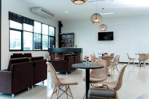 Modern lounge interior with beige chairs, black round tables, small flower vases, and travel suitcase in a bright waiting area with a bar counter photo