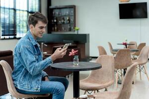 Young man using smartphone while sitting at modern lounge table with flower vase in relaxed waiting area with soft lighting and comfortable chairs photo