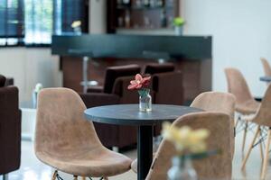 Modern cafe table with beige chairs and a small vase with artificial red flower in cozy indoor lounge with bar counter in soft background photo