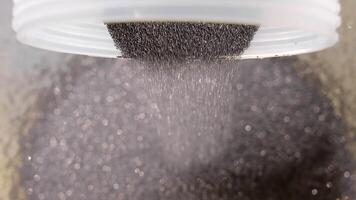Dark abrasive diamond powder falling from plastic container in controlled flow, Macro view of precise raw material handling in industrial tool production environment video