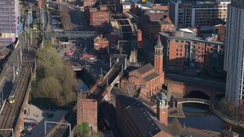Aerial view of Manchester, UK, showing a clock tower, railway bridge, moving trains, cars, red brick buildings, and modern structures in motion. video