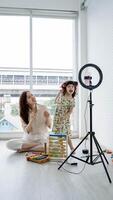 Mother and daughter having fun recording a together at home, smiling and dancing in front of a smartphone on tripod with toys scattered around. photo