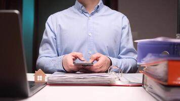 Real estate agent using smartphone in office with stack of documents and files video